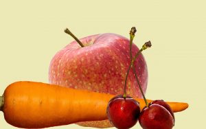 Ein Apfel, eine Karotte und Kirschen voreinander vor transparentem Hintergrund.