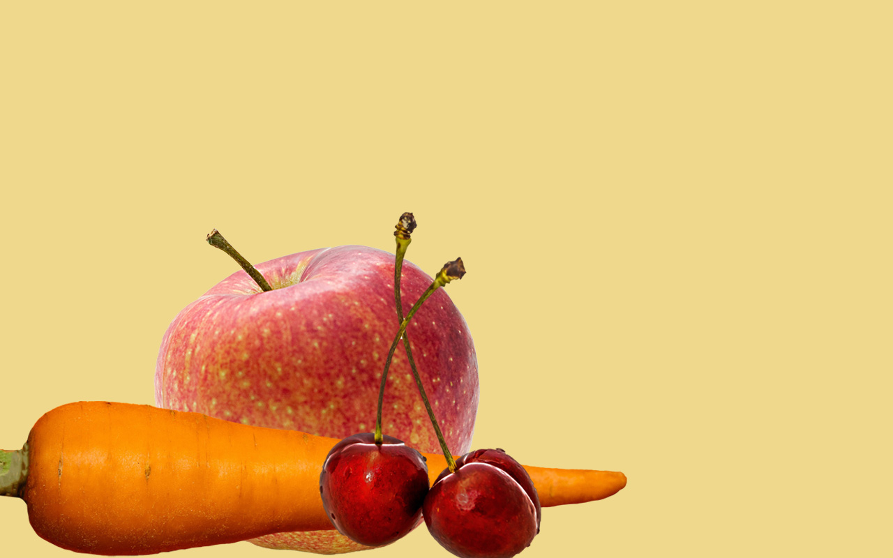 Ein Apfel, eine Karotte und Kirschen voreinander vor transparentem Hintergrund.