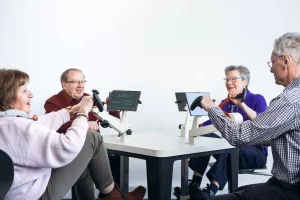 Vier Senioren sitzen an einem VitaTable mit vier Übungsgeräten für die Arme und vier Bildschirmen.